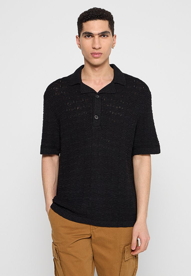 Schwarzes gestricktes Polohemd mit einem strukturierten Muster, kurzen Ärmeln und einem Knopfkragen. Der Stoff wirkt leicht und atmungsaktiv.