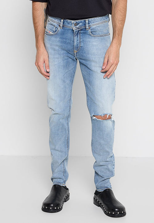 Hellblaue Jeans mit einem ausgewaschenen Finish, ausgestattet mit Rissen an den Knien und klassischem Fünf-Taschen-Design, getragen mit schwarzen Clogs.
