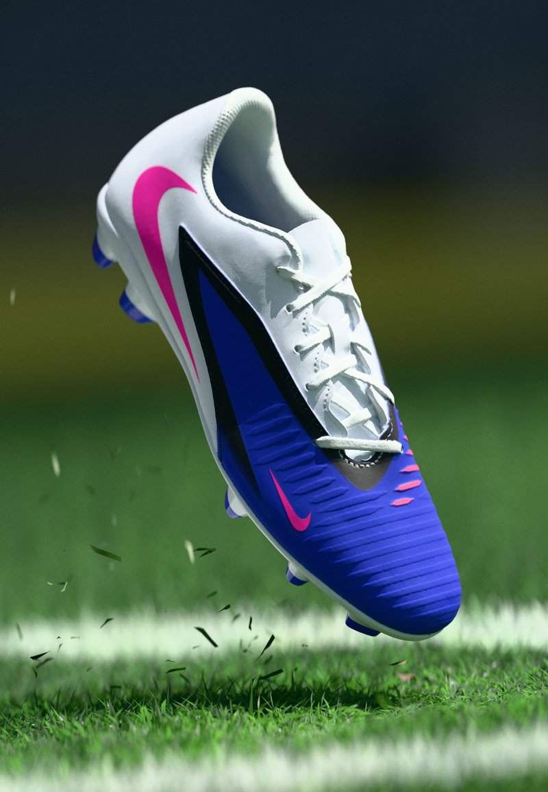 Weißer und blauer Fußballschuh mit pinkfarbenen Nike-Swooshes, der Gras auf einem grünen Feld in der Nähe einer weißen Linie aufwirbelt.