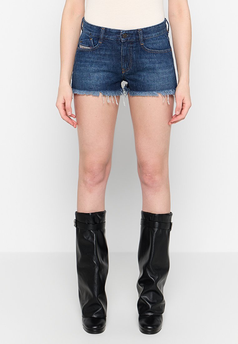 Dunkelblaue Jeansshorts mit ausgefranstem Saum, Fünf-Taschen-Design und kontrastierenden Nähten. Tragen Sie dazu hohe schwarze Lederstiefel.