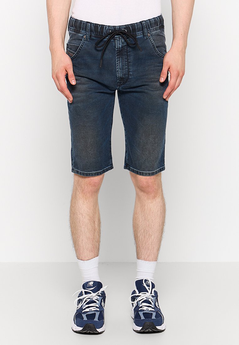 Dunkelblaue Jeansshorts mit einem Kordelzugbund, Fronttaschen und einem geraden Beinansatz, der knapp oberhalb des Knies endet. Kombiniert mit Sportschuhen.
