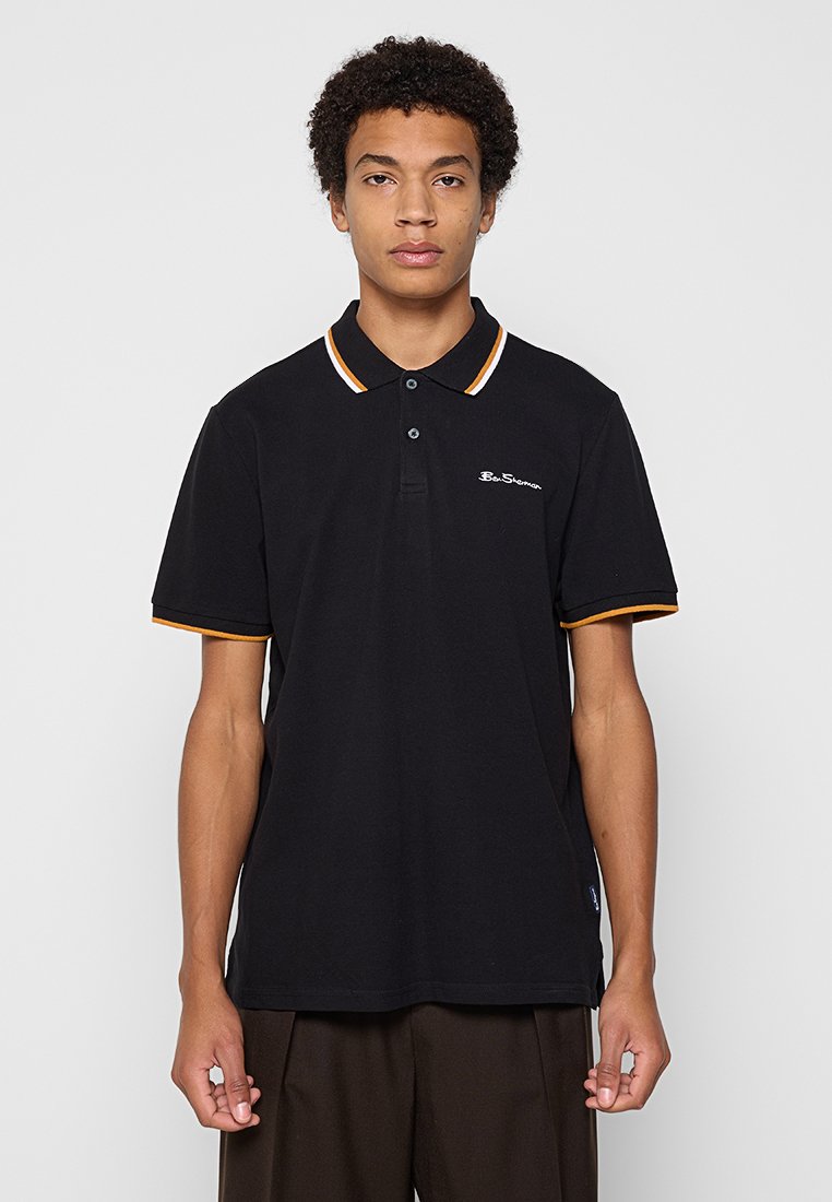 Schwarzes Poloshirt mit einer Knopfleiste mit zwei Knöpfen, geripptem Kragen mit weißen und orangefarbenen Streifen und einem kleinen, weißen Logo auf der Brust.