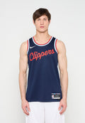 Mann trägt ein dunkelblaues Basketballtrikot der Los Angeles Clippers mit roten Buchstaben und weiße Shorts, steht vor einem einfarbigen weißen Hintergrund.