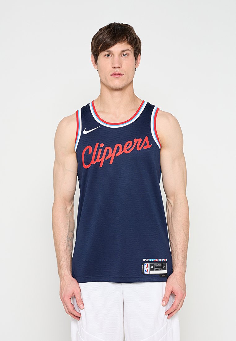 Mann trägt ein dunkelblaues Basketballtrikot der Los Angeles Clippers mit roten Buchstaben und weiße Shorts, steht vor einem einfarbigen weißen Hintergrund.