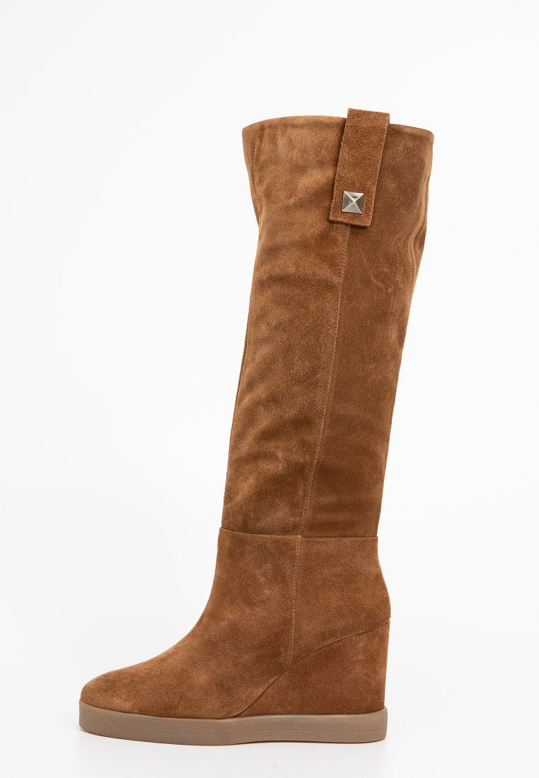 Hohe, braune Wedges aus Wildleder mit glatter Textur, ausgestattet mit einem breiten Bund und einem Metallelement am Riemen, konzipiert für einen sicheren Sitz.
