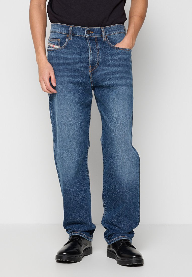 Lässige blaue Jeans mit einem ausgewaschenen Finish, Fünf-Taschen-Design, orangefarbenen Nähten und einem Knopfverschluss. Kombiniert mit polierten schwarzen Schuhen.