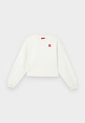 Weißes, kurz geschnittenes Sweatshirt mit langen Ärmeln, Rundhalsausschnitt und rotem Logo-Patch auf der linken Brust. Weicher Stoff und gerippte Bündchen.