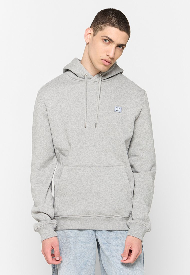 Grauer Hoodie mit Kängurutasche, Kapuze mit Zugband und einem kleinen blauen rechteckigen Logo auf der linken Brust. Weicher Stoff, lockere Passform.