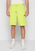 Mann in neon-gelben Diesel-Shorts mit Kordelzug, weißen Socken und weißen Turnschuhen, der vor einem schlichten Hintergrund steht.