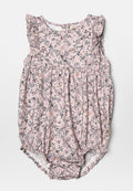 Rosa Jumpsuit mit Blumenmuster, Rüschenärmeln, gerafftem Bund und Druckknopfverschluss am Boden. Weicher Stoff mit subtiler Textur.