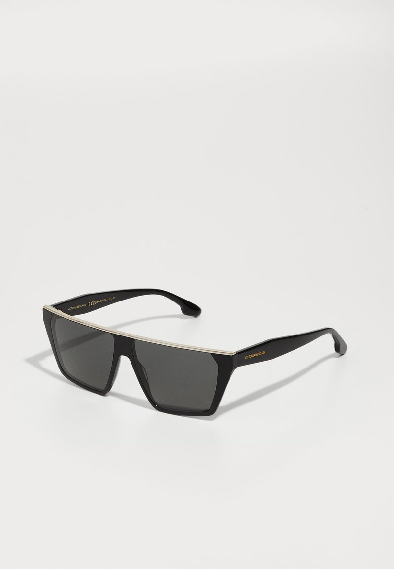 Schwarze quadratische Sonnenbrille mit grauen Gläsern, ausgestattet mit einem metallisch silbernen oberen Bügel und schlanken Bügeln. Das Gestell hat eine glänzende Oberfläche.