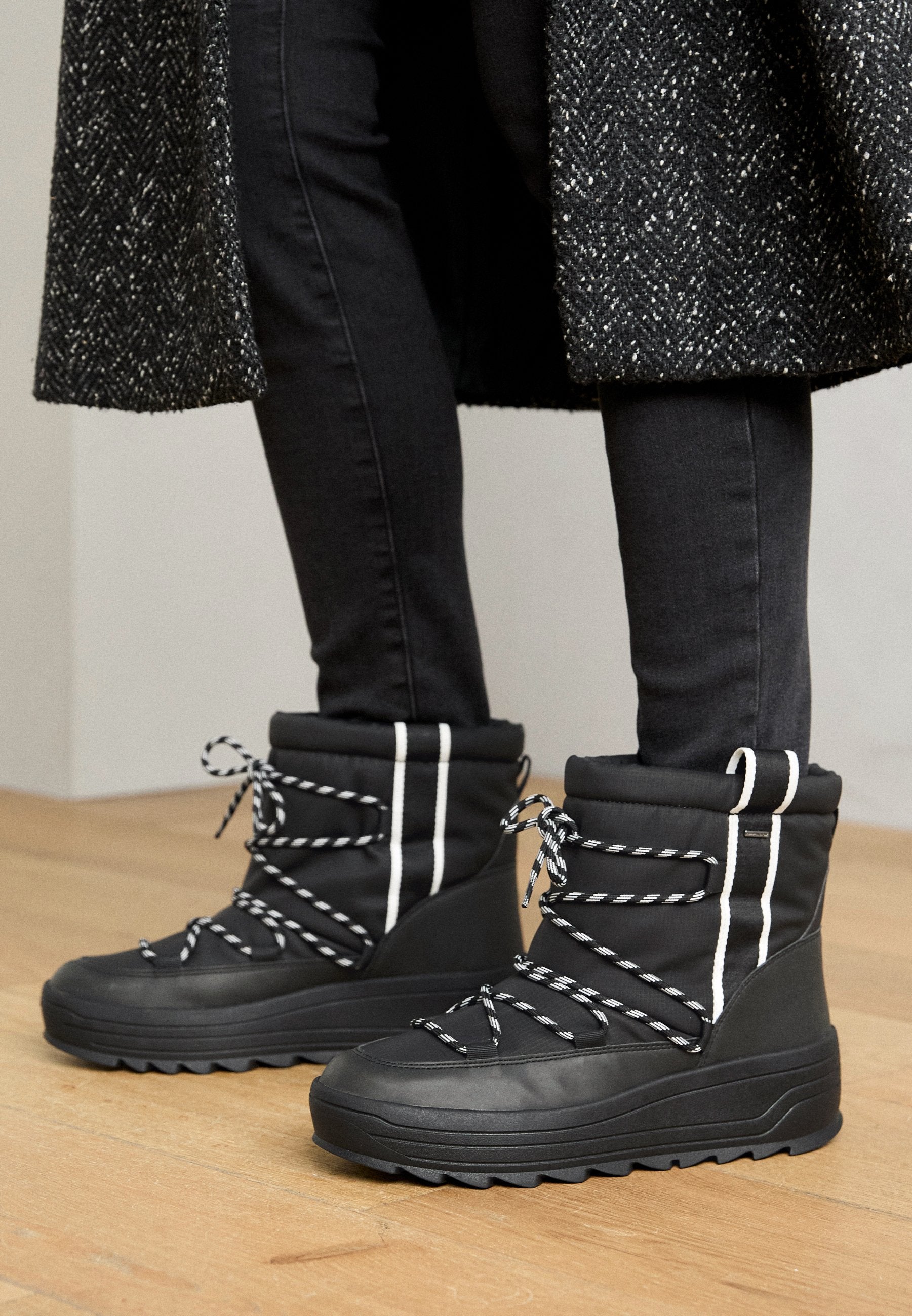 Schwarze wasserdichte Stiefel mit gepolstertem Schaft, weißen Streifenakzenten und schwarz-weißen Schnürsenkeln. Strukturiertes Gummisohle für Grip und Stabilität.