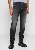 Mann trägt verwaschene schwarze Slim-Fit-Jeans und schwarze Plateauschuhe, steht vor einem schlichten grauen Hintergrund.