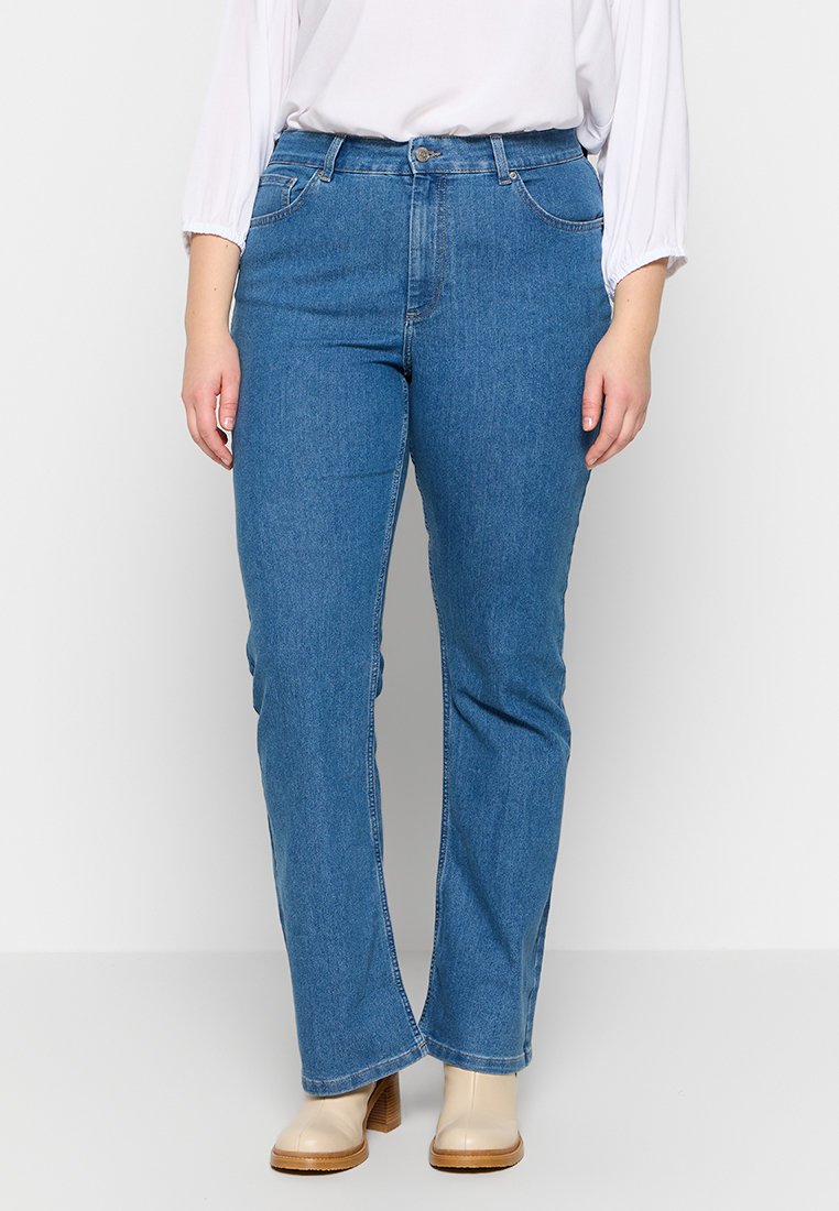 Blaue Jeans aus Denim mit geradem Bein, hoher Taille, Fronttaschen und einer dezenten, ausgewaschenen Textur. Kombiniert mit beigen Stiefeletten.