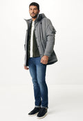 Grau mit Kapuze Parka aus strukturiertem Stoff, mit Knöpfen auf der Vorderseite und Außentaschen, kombiniert mit einem grünen Hemd, blauen Jeans und schwarzen Sneakers.