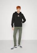 Schwarzer Kapuzenpullover mit Fronttasche und weißem "DIESEL"-Logo. Kombiniert mit olivgrünen Hosen und marineblauen Sneakers mit weißen Streifen.