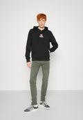 Schwarzer Kapuzenpullover mit Fronttasche und weißem "DIESEL"-Logo. Kombiniert mit olivgrünen Hosen und marineblauen Sneakers mit weißen Streifen.
