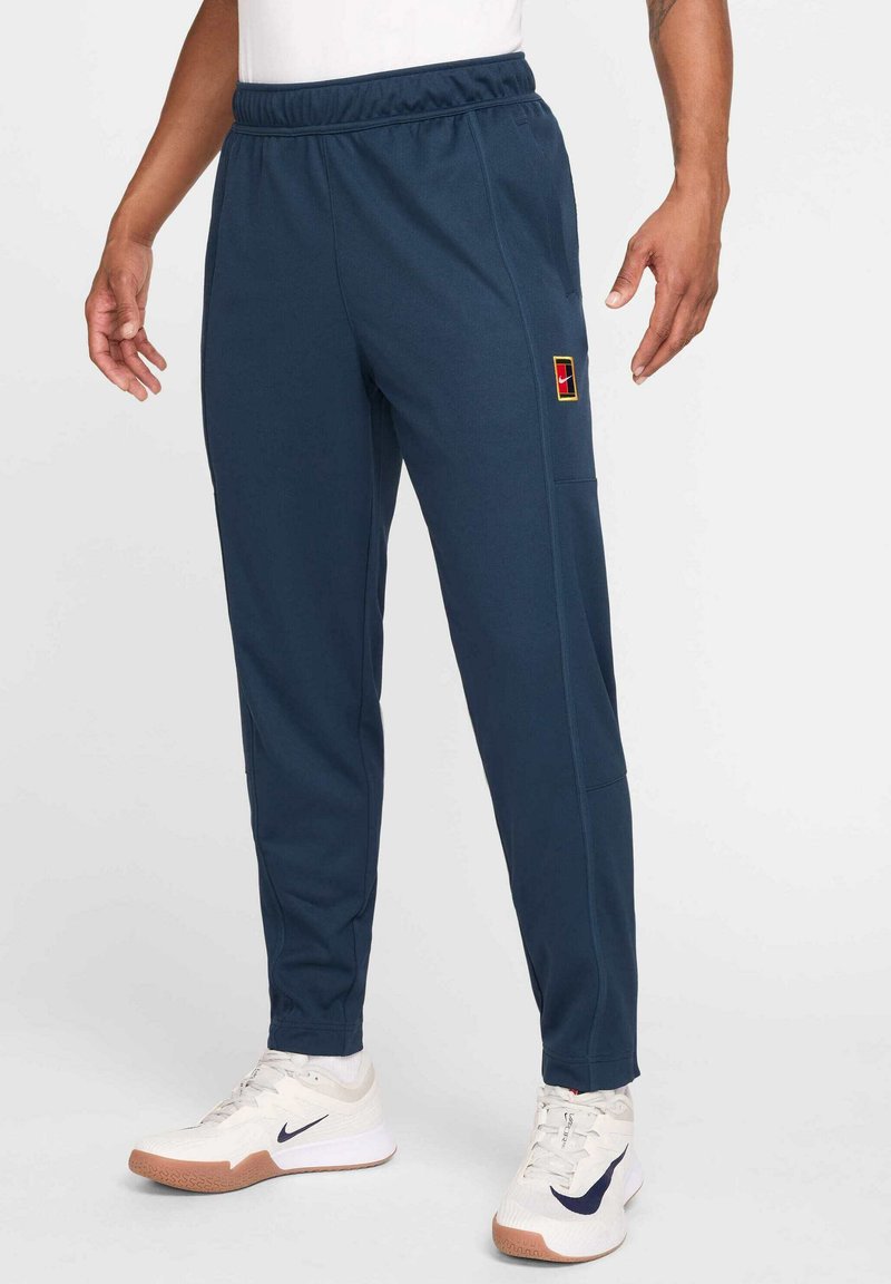 Marineblaue Jogginghose mit elastischem Bund, glatter Textur, Seitentaschen und einem mehrfarbigen Logopatch am linken Bein.