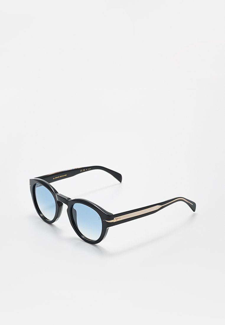 Schwarze runde Sonnenbrille mit blauen Verlaufsgläsern und feinem goldfarbenem Streifendetail an den Bügeln, auf einer weißen Oberfläche präsentiert.