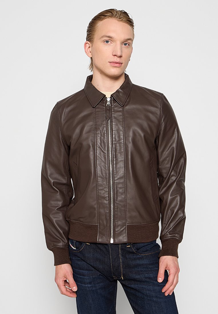 Braune Lederbomberjacke mit Reißverschluss vorne, gerippten Bündchen und Kragen; glatte Textur und taillierte Passform; kombiniert mit dunklen Jeans.