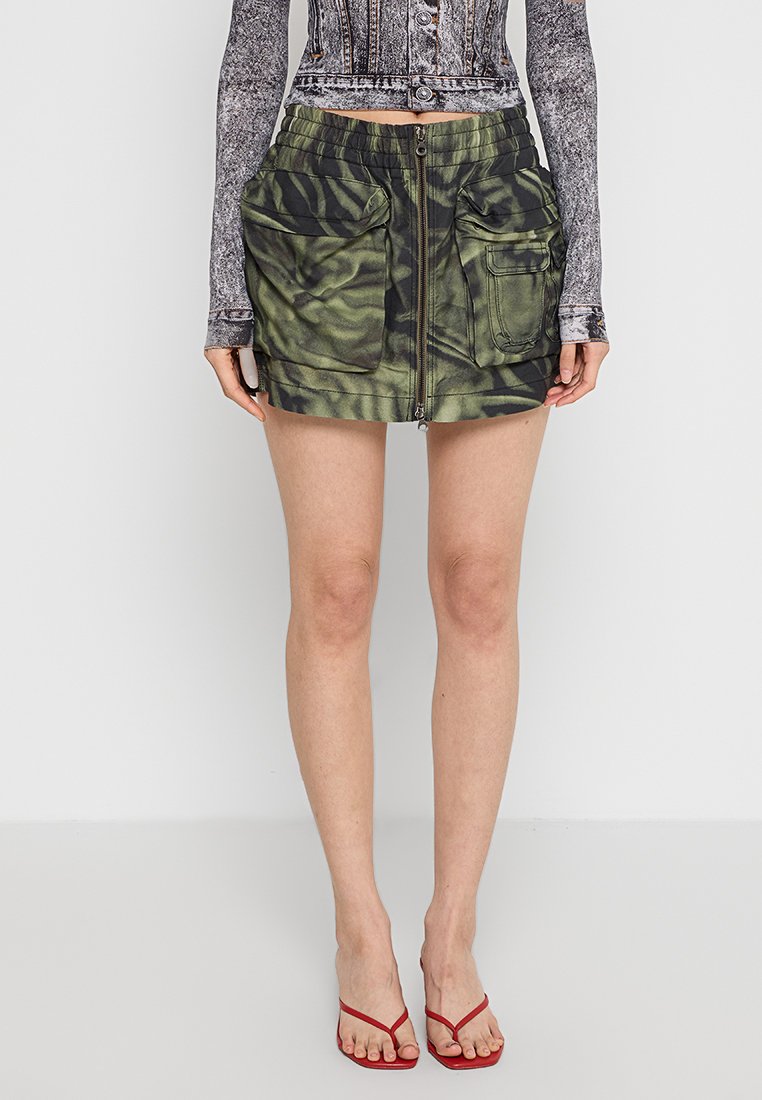 Minirock mit Camouflage-Muster in Grün, ausgestattet mit einem Frontreißverschluss und zwei großen Seitentaschen. Hergestellt aus leichtem Stoff mit entspanntem Schnitt.