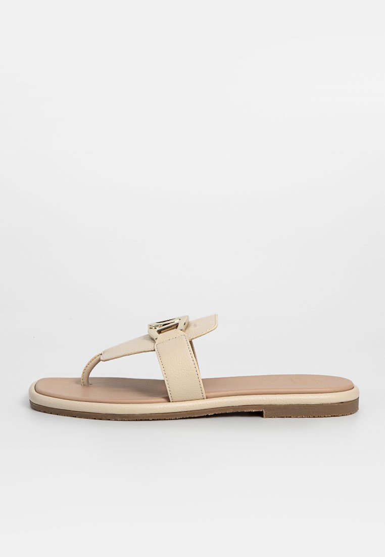 Beige Zehentrenner mit einem glatten Lederriemen und einem metallischen Akzent. Die Sohle ist flach und hat eine hellfarbige Gummibasis.