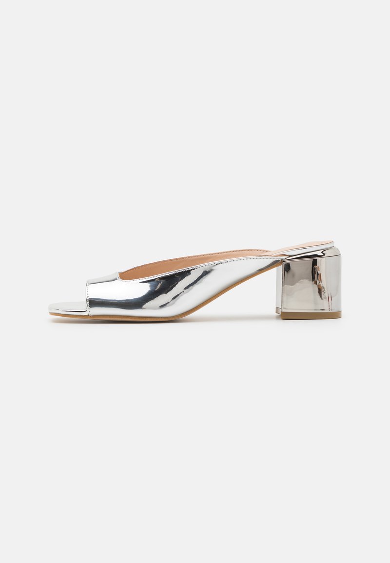 Metallisch silberne offene Absatzmules mit Blockabsatz. Glatte, reflektierende Oberfläche; minimalistisches Design mit geschwungenem Silhouette.