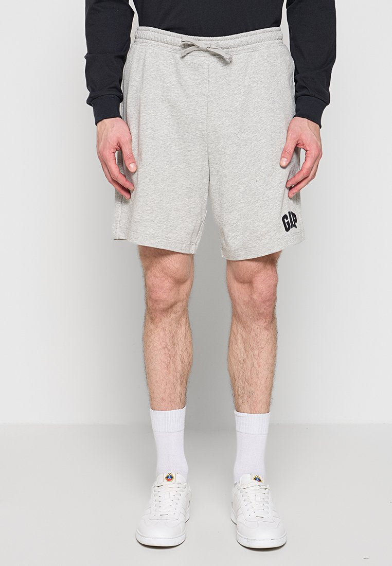 Mann trägt hellgraue Shorts mit Kordelzug und "GAP"-Logo, weiße Socken, weiße Turnschuhe und ein schwarzes Langarmshirt und steht vor weißem Hintergrund.