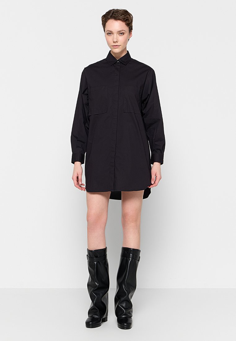 Schwarzes Langarmhemdkleid mit durchgehendem Knopfverschluss, zwei Brusttaschen, geradem Schnitt und einem leicht längeren hinteren Saum.