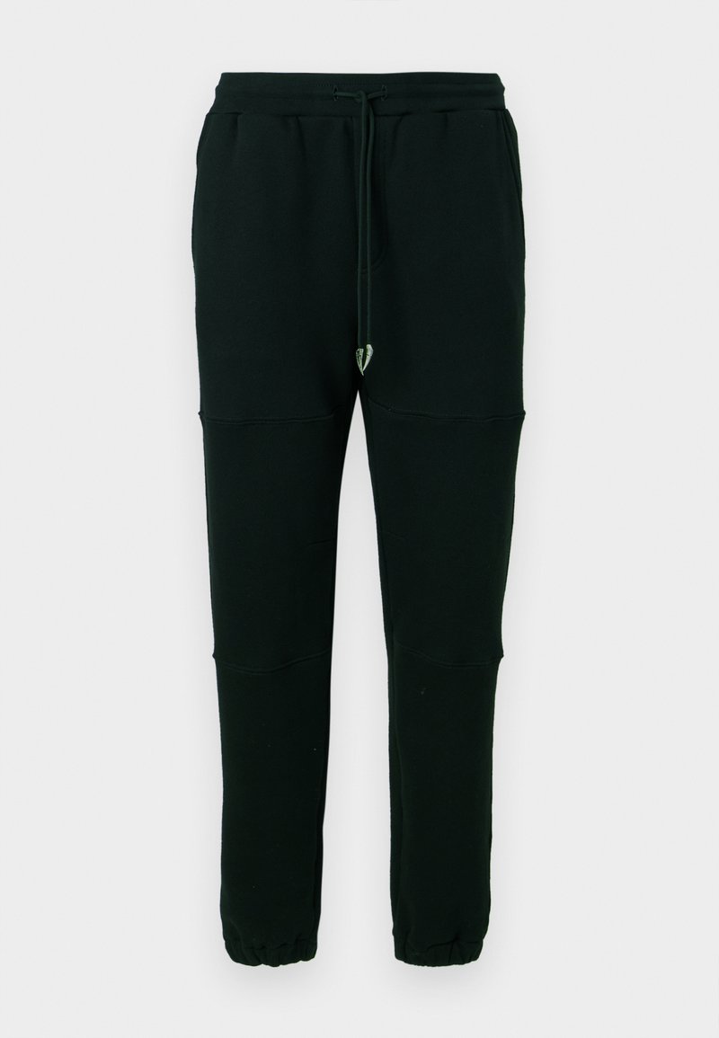 Schwarze, schmal geschnittene Jogginghosen mit elastischen Bündchen, seitlichen Taschen, einem Kordelzugbund und Nahtdetails an den Knien auf einem schlichten Hintergrund.