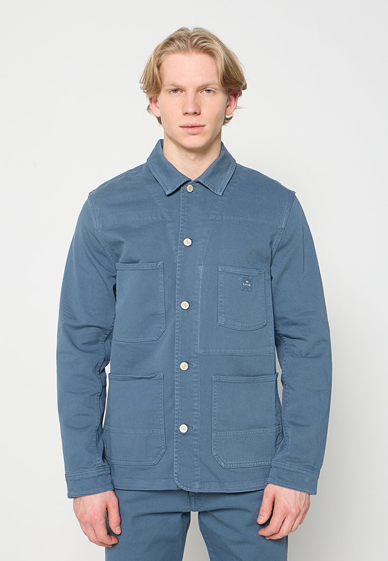 Blaue Baumwolljacke mit Kragen, vier Fronttaschen und Knopfverschluss. Verfügt über eine strukturierte Oberfläche und sichtbare Nahtdetails.