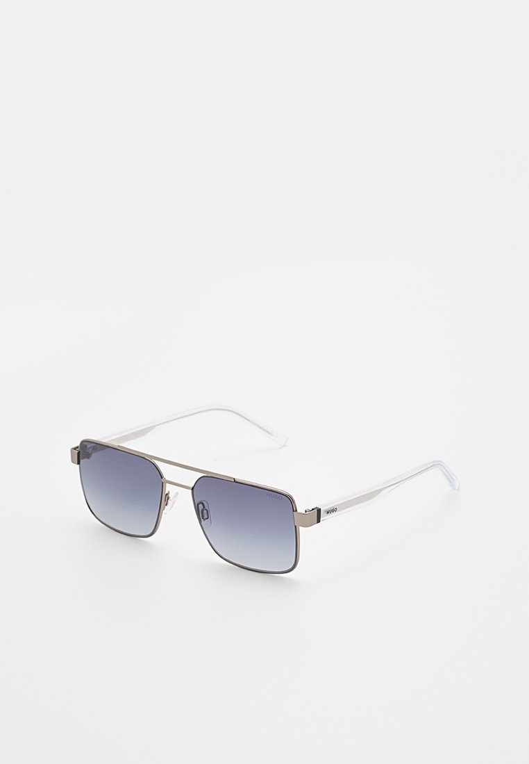 Sonnenbrille mit Metallrahmen, rechteckigen blauen Verlaufsgläsern und transparenten Kunststoffbügeln, liegend auf einer weißen Oberfläche.