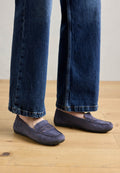 Lila Wildleder-Lokschuhe mit gestepptem Nahtdetails und einer flachen Gummisohle, getragen mit weit geschnittenen blauen Jeans, die einen lässigen Stil auf einem Holzfußboden zeigen.