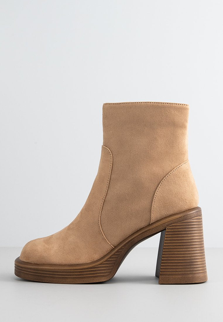 Beiger Wildleder-Stiefelette mit abgerundeter Zehenpartie, hohem, gestapeltem Absatz mit horizontalen Streifen und einer glatten, matten Oberfläche.