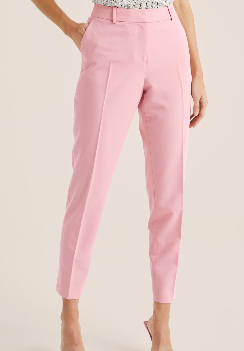 Rosa maßgeschneiderte Hose mit glatter Textur, schlankem Schnitt, hoher Taille und Vorderfalte. Getragen mit einem gemusterten Oberteil.