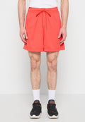 Mann trägt leuchtend rote Sportshorts mit Kordelzug, weiße Socken und schwarze Turnschuhe, steht vor einem schlichten weißen Hintergrund.