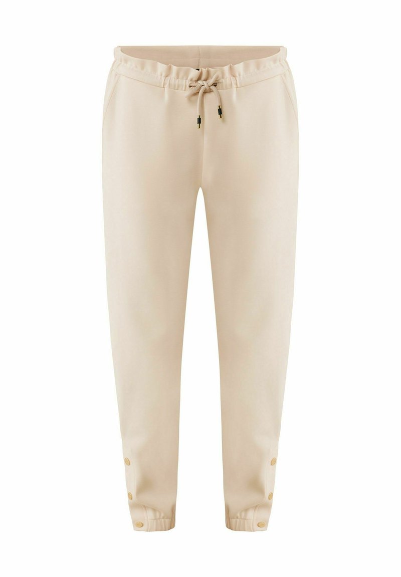Beige Jogginghosen aus weichem Stoff, mit einem elastischen Bund und einer Kordel sowie Druckknopfakzenten an den Knöcheln.