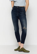 Dunkelblaue Skinny-Jeans mit weit aufgerissenem Knie, hoher Taille und leichter Ausbleichung. Kombiniert mit einem grauen Crop-Top und grünen Slippern.