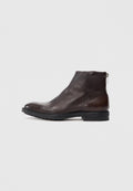 Dunkelbraunes Leder-Ankle-Boot mit seitlichem Reißverschluss, schwarzer Sohle mit Profil und niedrigem Absatz, im Profil auf weißem Hintergrund dargestellt.