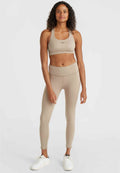 Beige Sport-BH und Leggings aus dehnbarem Stoff. Der BH hat einen breiten Träger und ein Logo. Enganliegende, hochtaillierte Leggings reichen bis zu den Knöcheln.