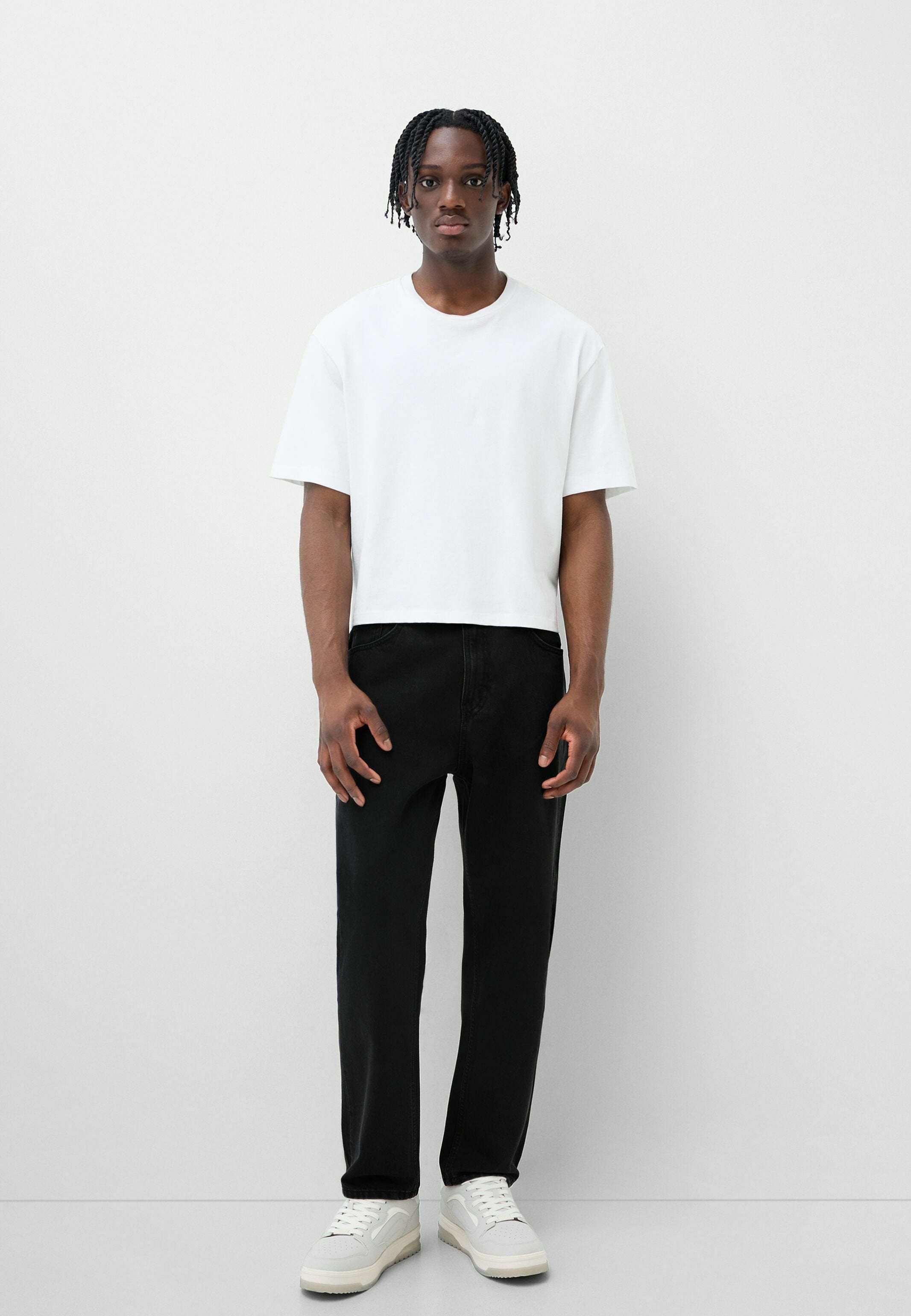 Weißes Baumwoll-T-Shirt mit kurzen Ärmeln, entspannte Passform, kombiniert mit schwarzen Jeans mit geradem Bein und weißen Sneakers mit strukturierten Sohlen.