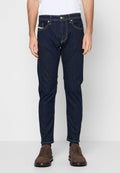Dunkelblaue Jeans mit schmaler Passform, gelben Nähten, Fünf-Taschen-Design und Knopfverschluss. Kombiniert mit braunen Schuhen.