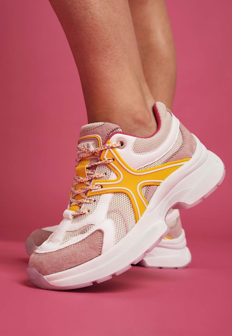 Rosa und weiße Sportschuhe mit einem Obermaterial aus Mesh, Wildlederakzenten, gelben Details und strukturierten Schnürsenkeln. Dicke weiße Sohle mit einem klaren Abschnitt.