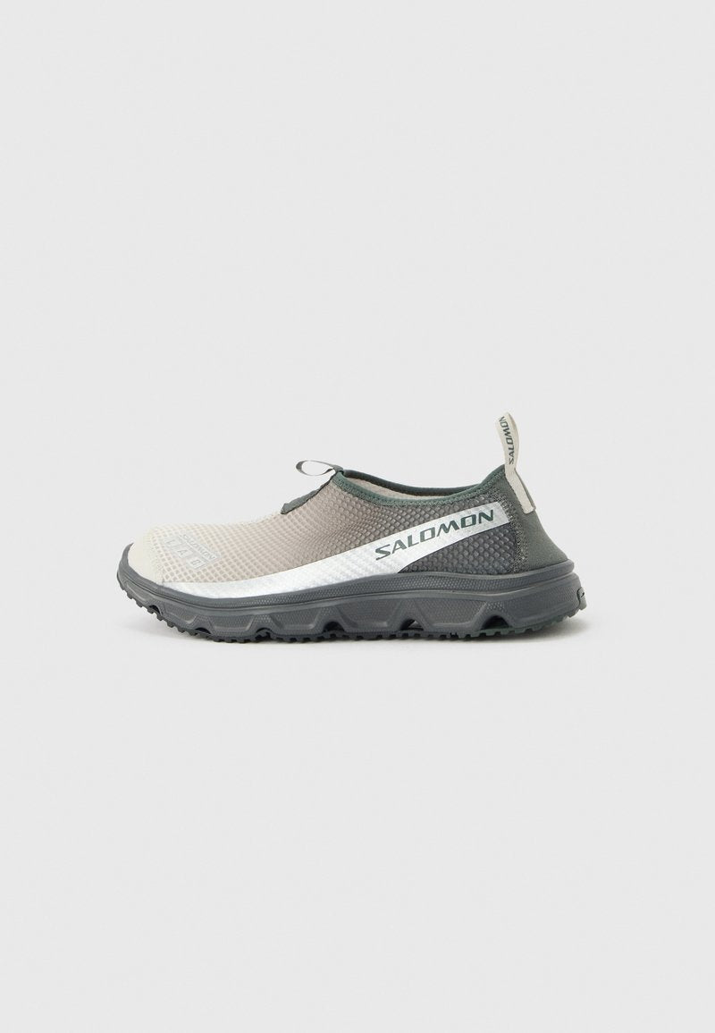 Hellgrauer und schwarzer Salomon Trail-Schuh zum Hineinschlüpfen mit profilierter Sohle und Zuglaschen an Zunge und Ferse, seitliches Logo sichtbar.