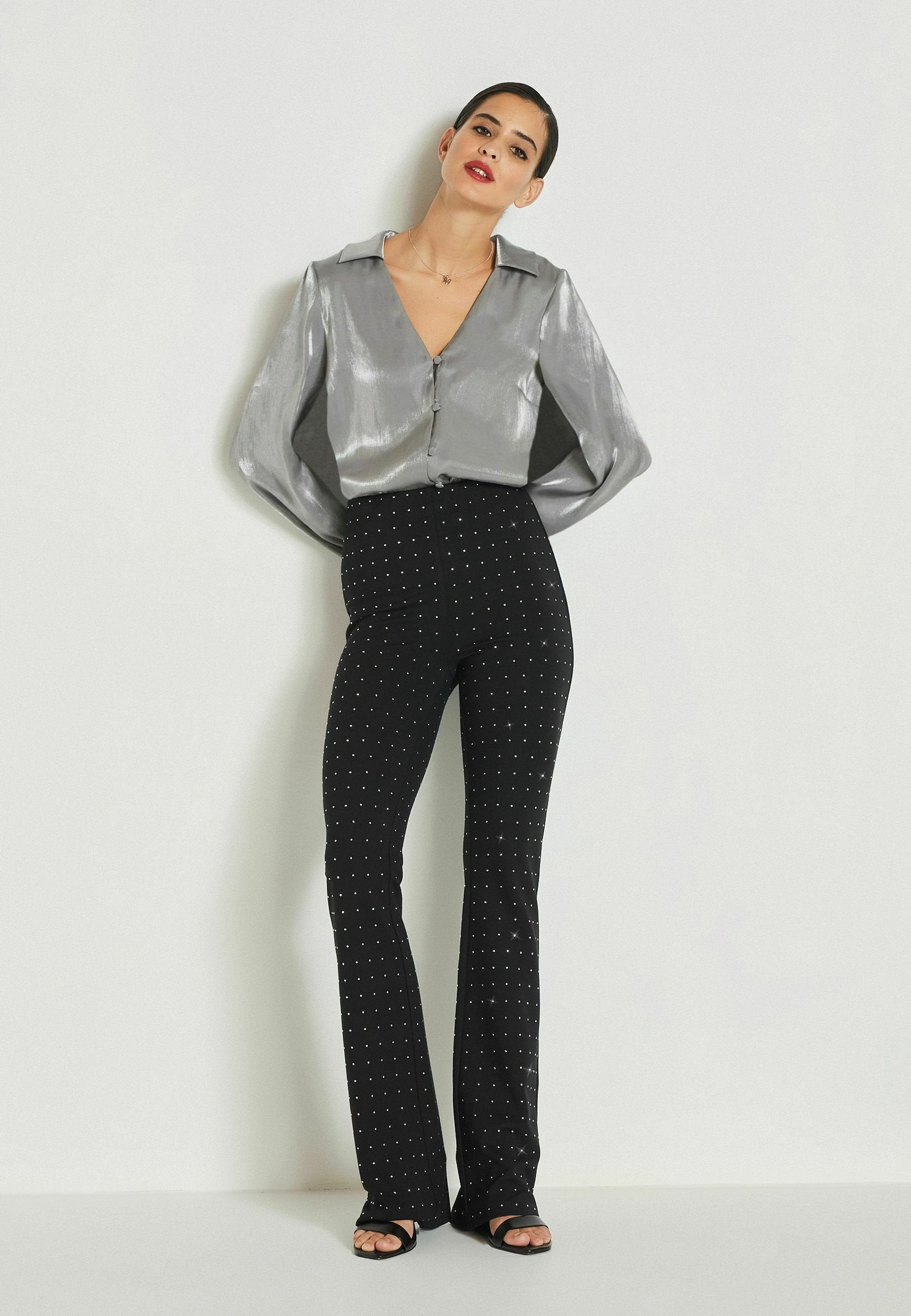 Schimmernde silberne Bluse mit Knopfleiste, V-Ausschnitt und weiten Ärmeln, kombiniert mit schwarzen, weit geschnittenen Hosen mit weißen Polka-Dots.
