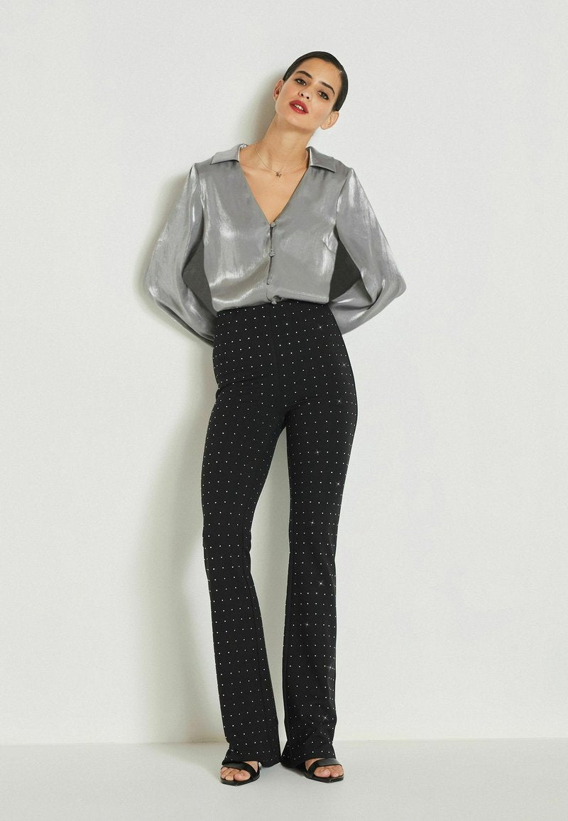 Schimmernde silberne Bluse mit Knopfleiste, V-Ausschnitt und weiten Ärmeln, kombiniert mit schwarzen, weit geschnittenen Hosen mit weißen Polka-Dots.