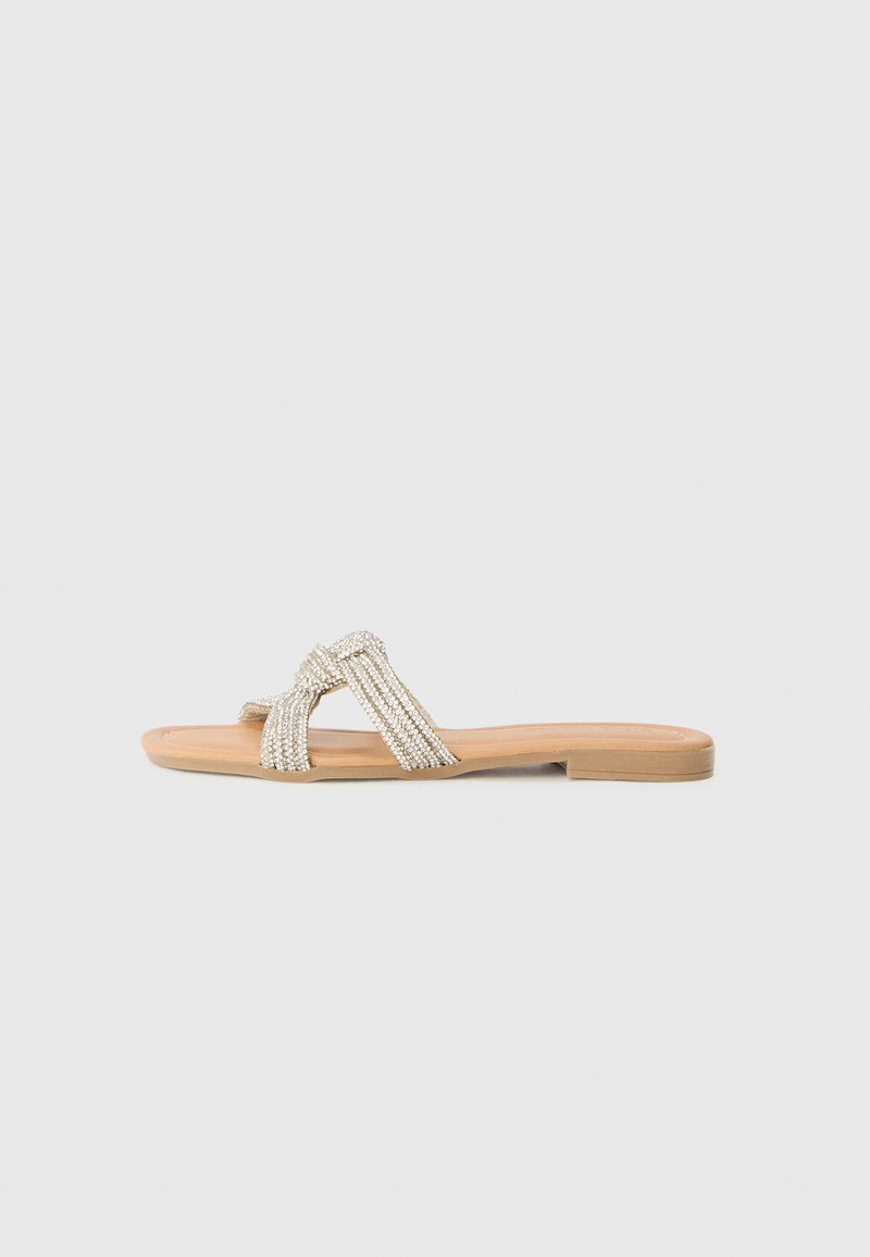 Perlenverzierte flache Sandalen mit einer braunen Sohle. Sie verfügen über ein überkreuztes Riemendesign aus funkelnden silbernen Perlen, das ein strukturiertes Aussehen bietet.
