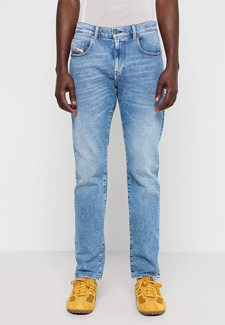 Helle blaue Jeans mit geradem Schnitt, ausgestattet mit fünf Taschen, kontrastfarbigem Nähten und einer ausgewaschenen Optik. Getragen mit gelben Sneakers.