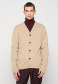 Beiger Cardigan aus weichem Material mit V-Ausschnitt, fünf schwarzen Knöpfen sowie gerippten Bündchen und Saum. Wird über einem burgunderroten Rollkragenpullover getragen.