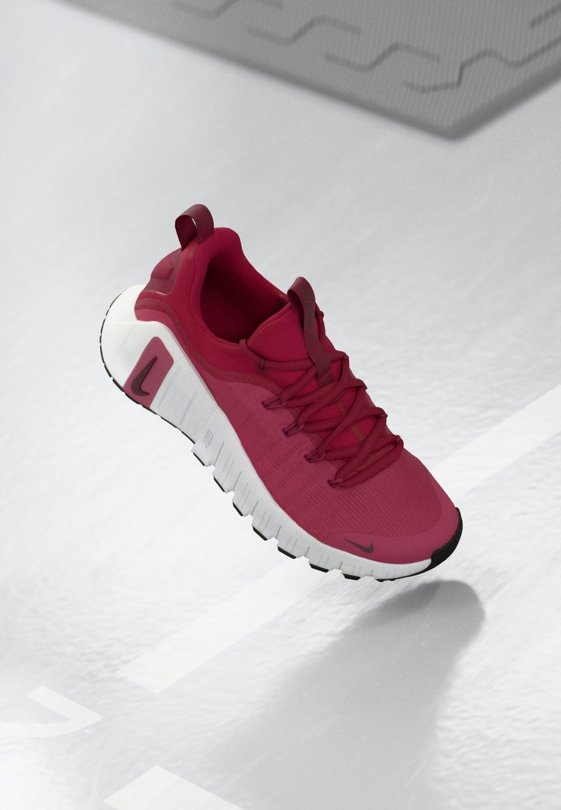 Roter Turnschuh mit strukturiertem Obermaterial, Schnürsenkeln und einer dicken weißen Sohle. Verfügt über eine kontrastierende schwarze Zehenkappe und ein Logo an der Seite.